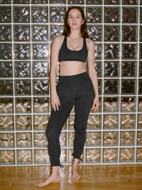 Model in black Star Bra with medium support, paired with matching leggings, standing confidently against a glass block wall.