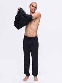 Model pulling on a top while wearing Stratus Sweatpant in Black, heavyweight and ultra-soft fabric for comfort.