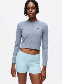 Model posing in Sugar Cardigan in Blue with soft cotton cashmere and hand-embroidered OV signature.