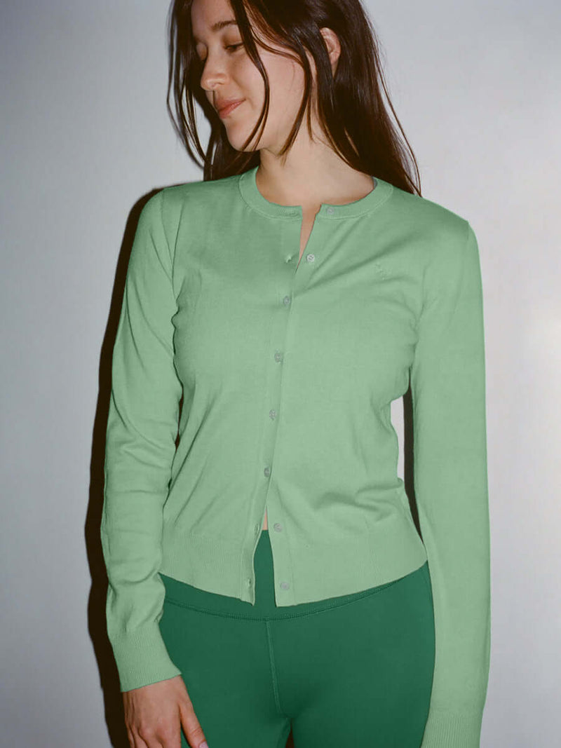Model smiling while wearing Sugar Cardigan in light green, soft cotton cashmere with hand-embroidered details.