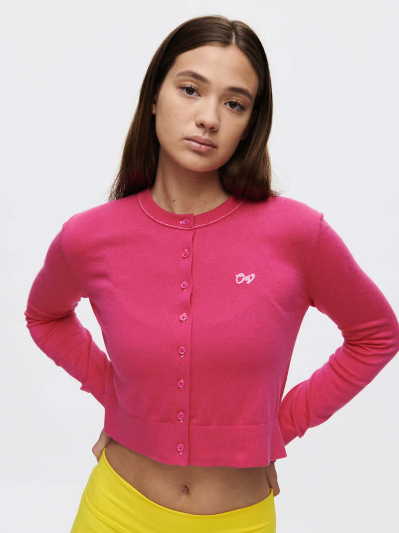 Model wearing Sugar Cardigan in bright pink, featuring hand-embroidered OV signature and a cropped fit.
