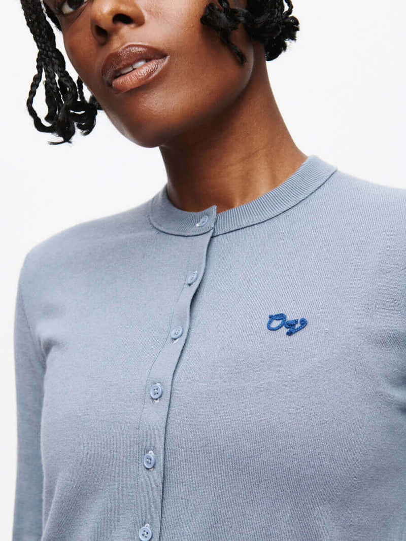Close-up of model wearing Sugar Cardigan in Light Blue, featuring hand-embroidered OV signature.