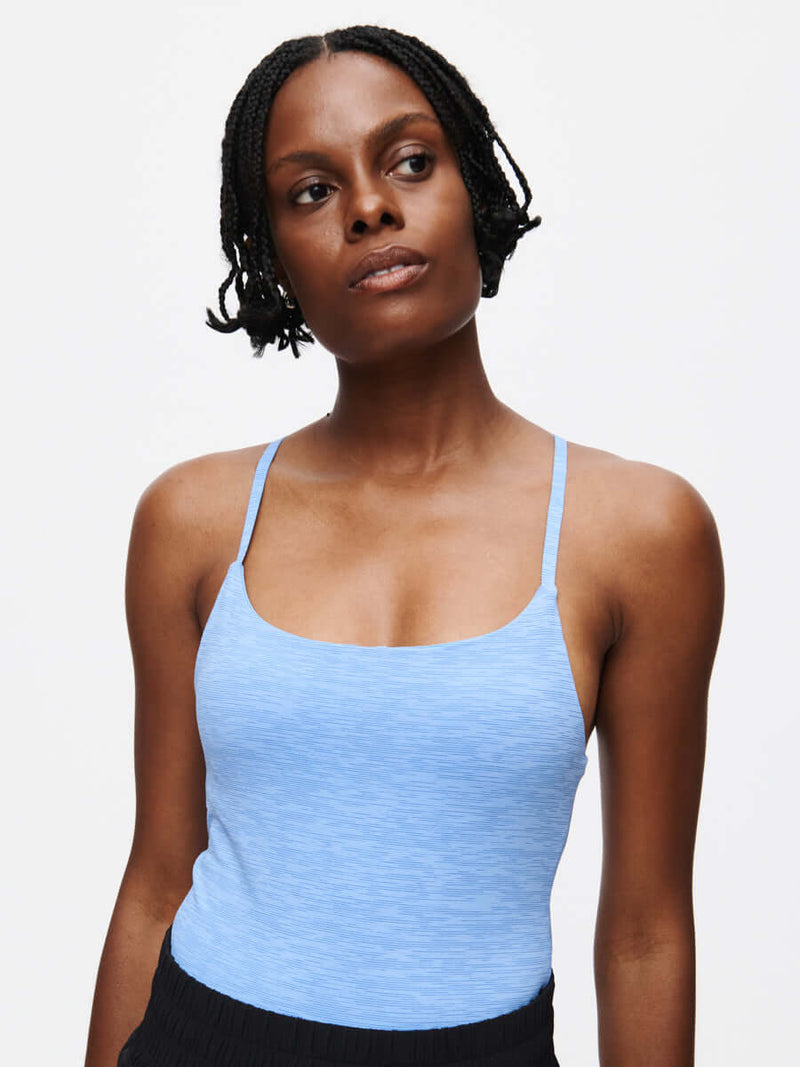Model wearing TechSweat Move Free Tank in light blue, featuring adjustable racerback straps.