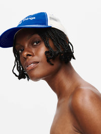 Model wearing a stylish Doing Things Trucker Hat in blue, with a trendy casual vibe.