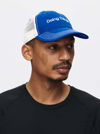 Trucker Hat featuring a blue and white design, model with the Doing Things brand.