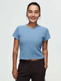 Model smiling in Waffle Baby Tee in Blue, fitted style with a soft, textured knit fabric.