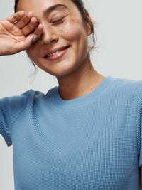 Model smiling in Waffle Baby Tee, soft cotton waffle knit in light blue, for everyday wear.