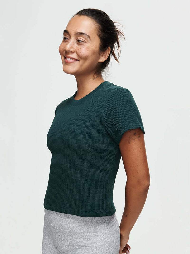 Model smiling in Waffle Baby Tee in Dark Green, fitted style with soft waffle knit fabric.