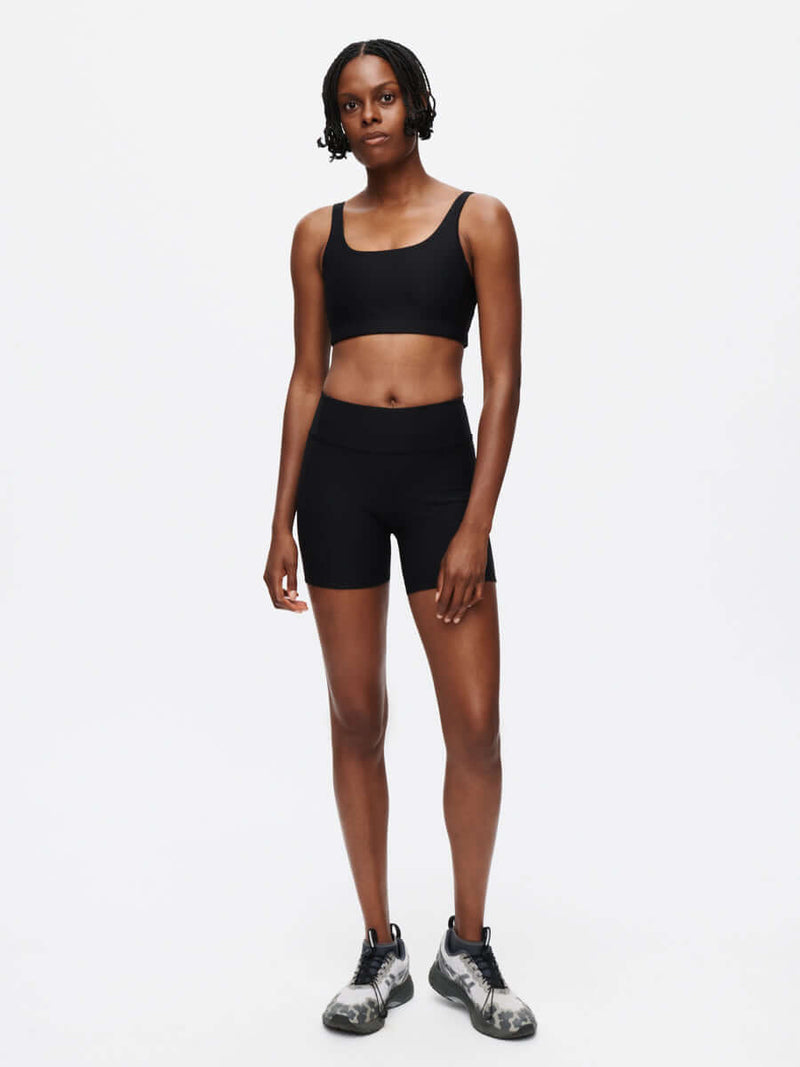 Warmup 5" Short model wearing a sleek black outfit with a sculpted-fit design and waistband pocket.