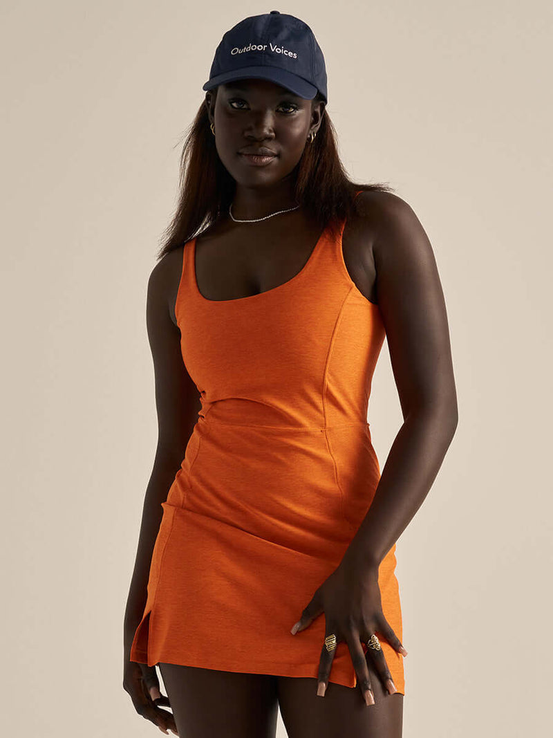 Model posing in Warmup Dress in Bright Orange, showing a fitted shape and scoop neckline.