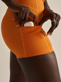 Close-up view of Warmup Dress in Orange, showing side pocket holding a phone for activewear convenience.