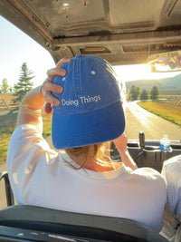 Rear view of a person wearing Washed Hat in Blue, featuring the phrase Doing Things in white stitching.