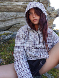Model sitting in a natural setting wearing Windbreaker in mineral blue plaid, featuring a hood and lightweight fabric.