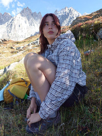 Model sitting in nature wearing Windbreaker in mineral blue plaid, featuring a lightweight wind- and water-resistant finish.